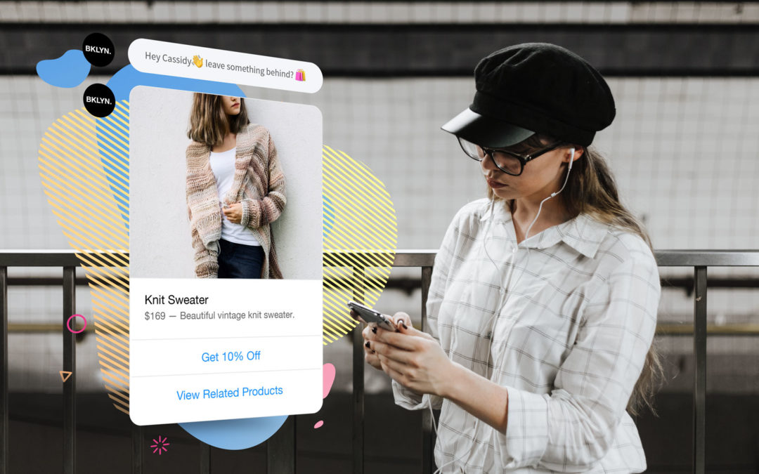 A young woman wearing a black cap stands on an empty subway platform, looking at her phone. In the space beside her floats a chat conversation from a brand reminding her about the knit tan cardigan she was browsing on their site moments before she switched screens to look up her train's schedule.