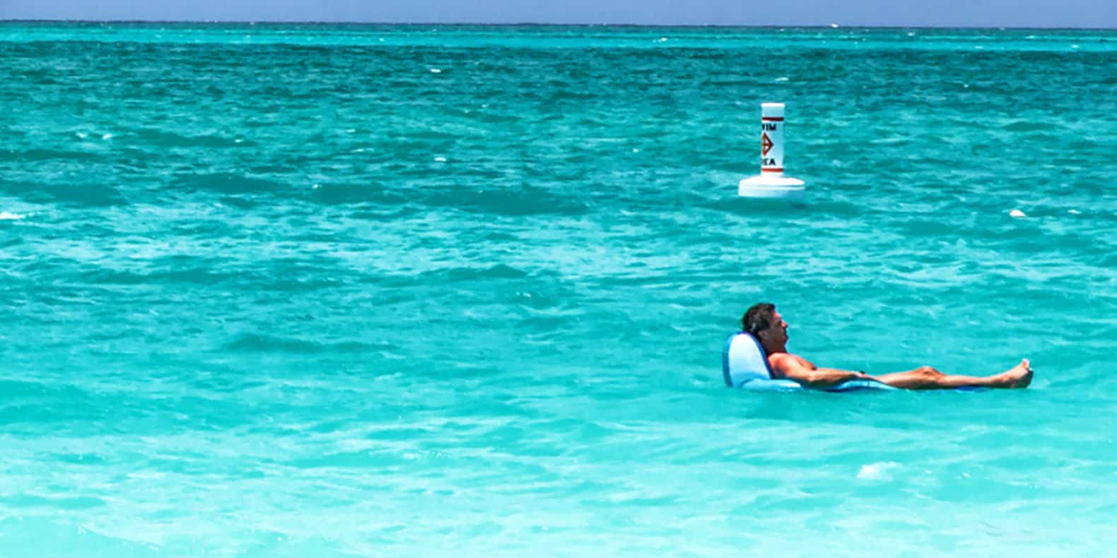 Photo of Billy McFarland floating on an inflatable recliner drifts in a turquoise blue ocean.