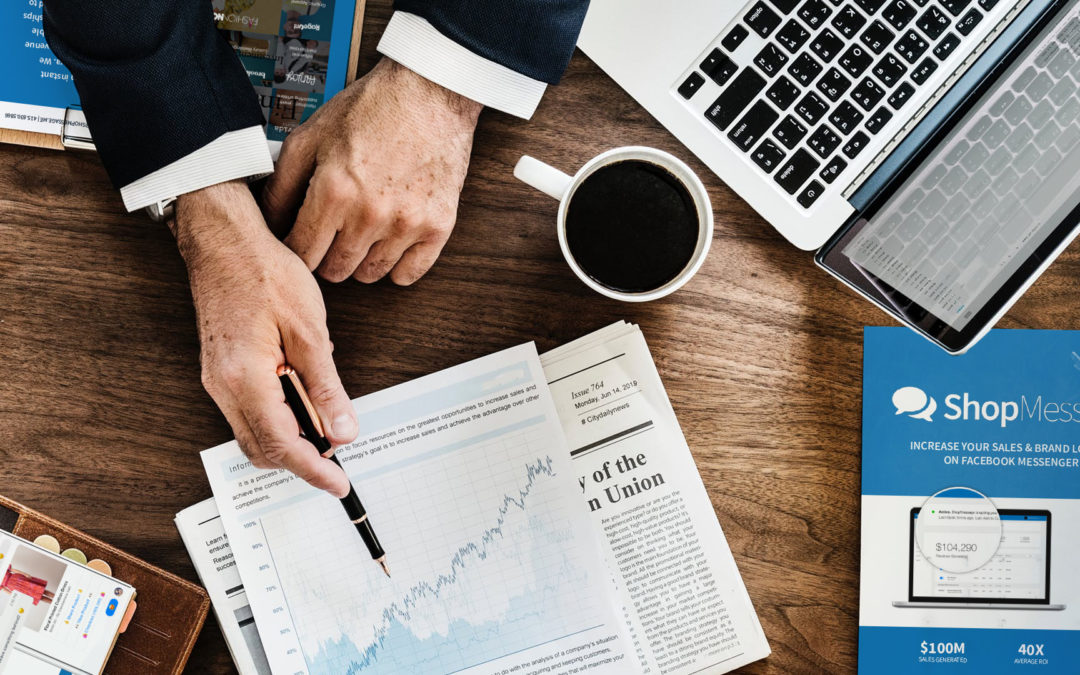 Overhead view of businessman pointing across the table at a chart trending upwards. Papers scattered on the table show off ShopMessage's one-sheet.